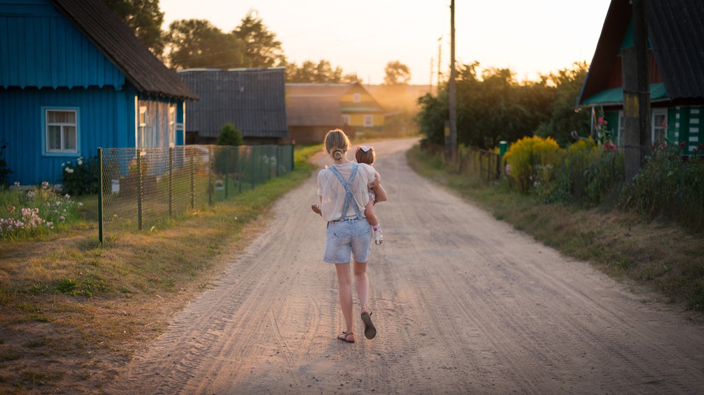 Woman holding baby and walking away down a dirt road.