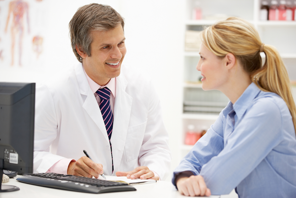 Male doctor chatting to female patient behind desk