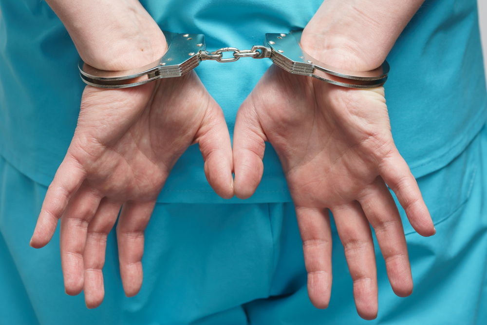 a handcuffed doctor in blue scrubs