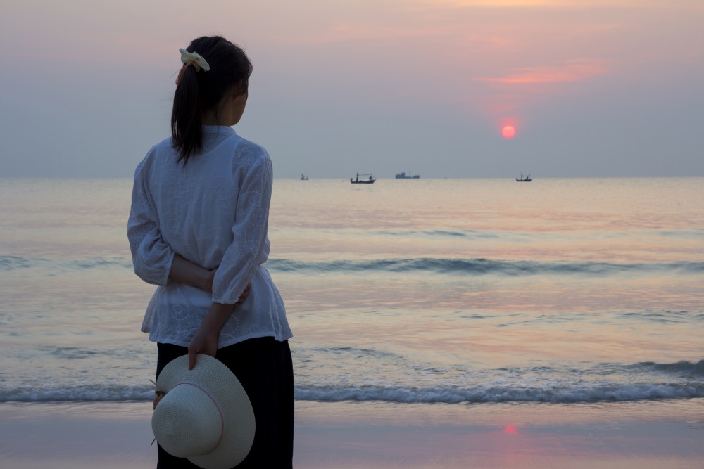 woman on a beach looking at a sunset