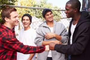 A group of young men smiling and greeting each other.