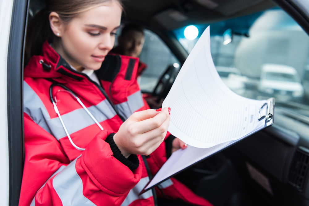 female paramedic sitting in ambulance and looking at clipboard