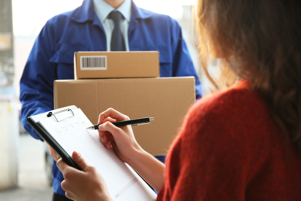 Young woman signing documents after receiving parcels from courier, closeup