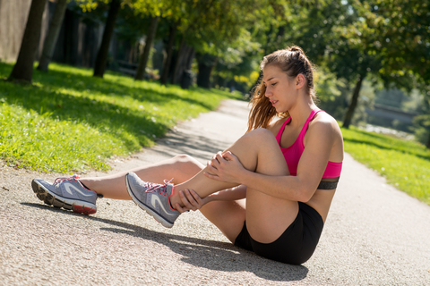 A young woman runner sits on the ground holding her leg