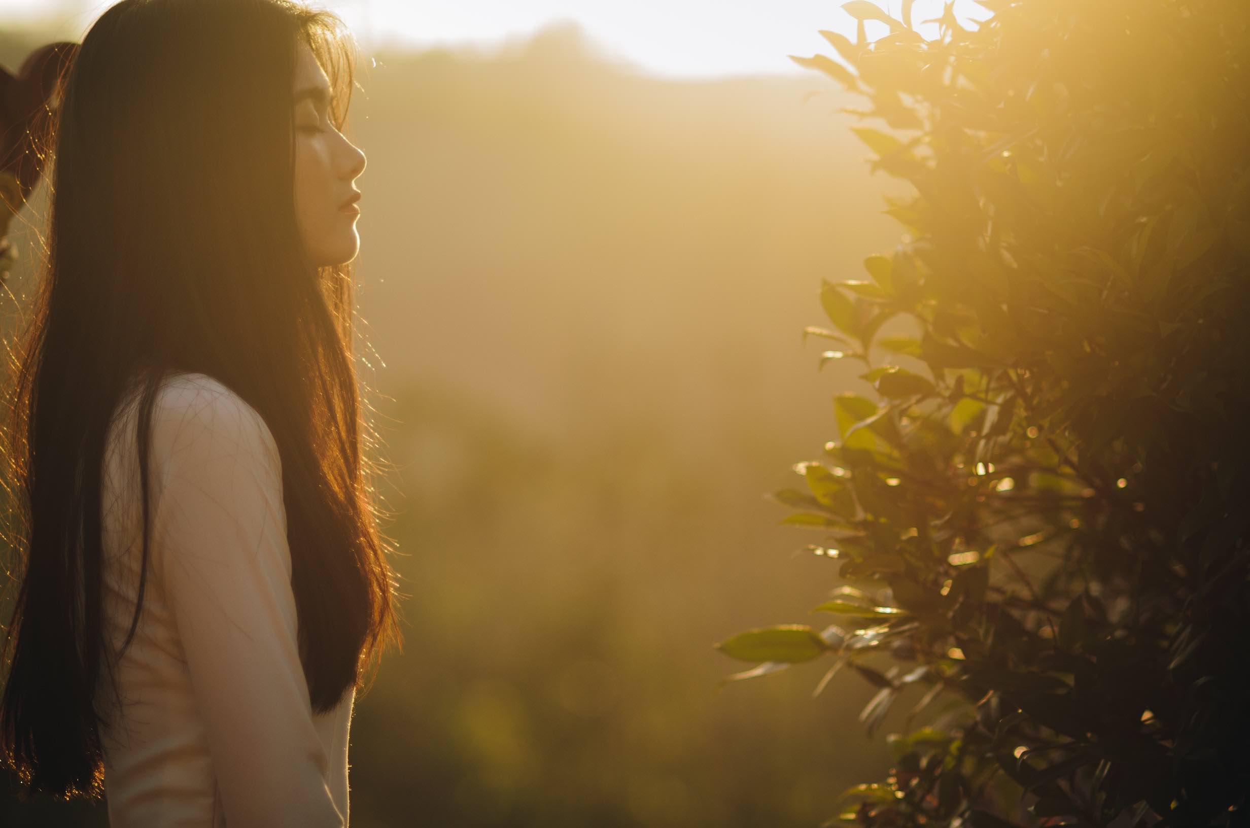 Woman standing with eyes closed, in profile and in the sun.