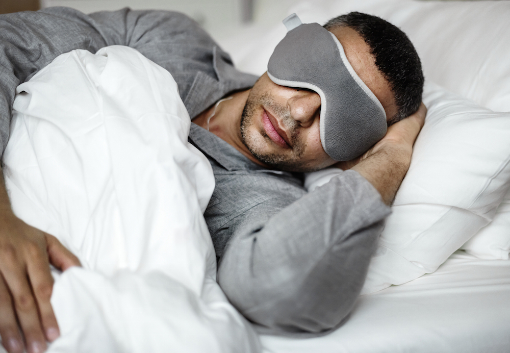 a man wearing a sleep mask sleeping in a bed