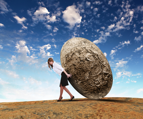 A woman balancing a boulder against her back.