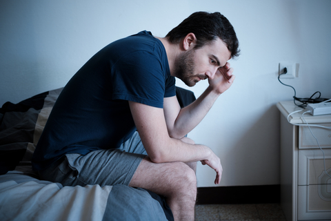 Depressed man sitting on bed.