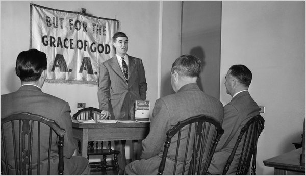 Black and white image of men in suits at a table under a sign reading "BUT FOR THE GRACE OF GOD A.A."