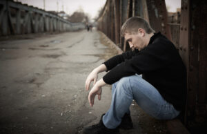 pensive young man sitting down on the street