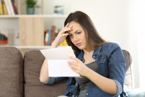 Concerned woman reading bad news in a letter sitting on a couch at home