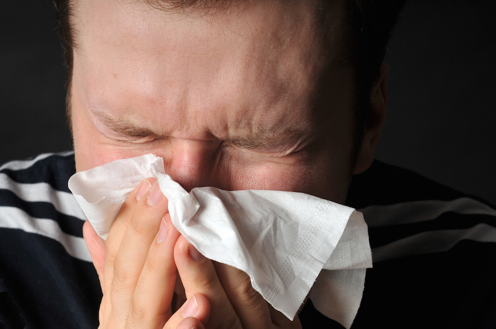 man blowing nose into tissue.