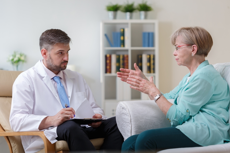 A patient and doctor sit on couches talking to each other.