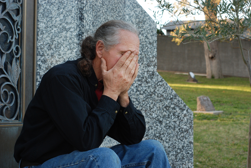 Man sits at gravesite with head in hands.