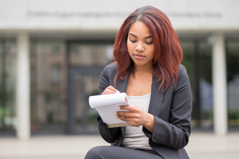 Young woman writing in a notebook and sitting outside.