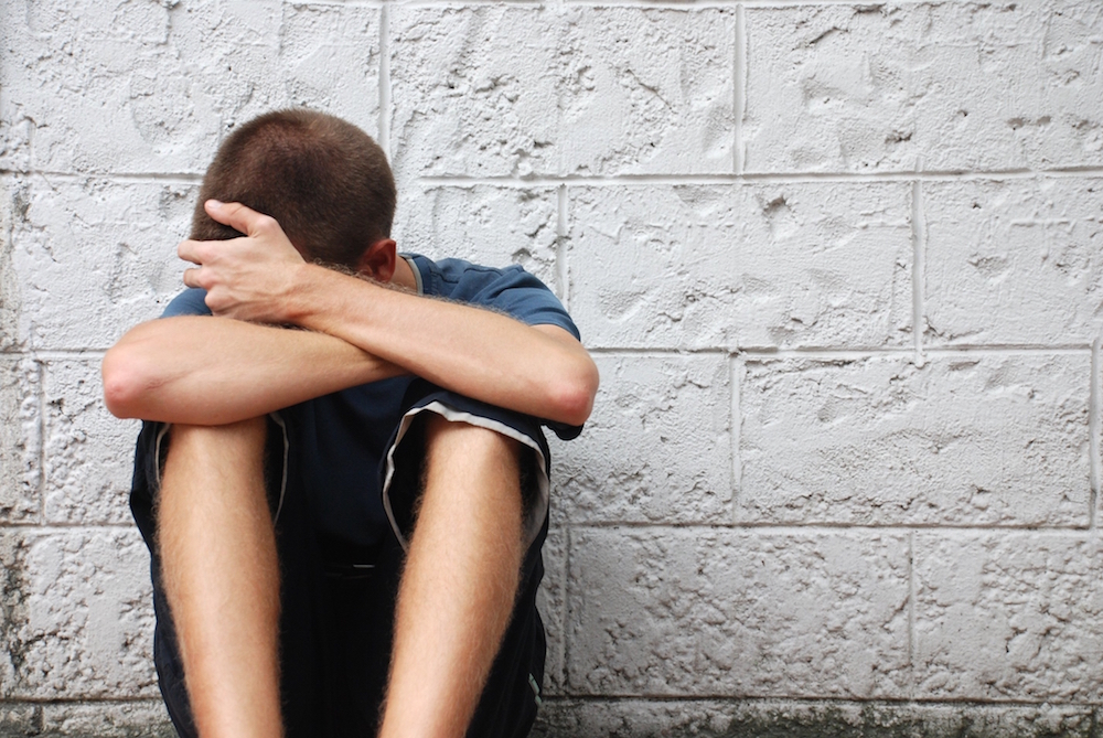 sad man sitting against a wall