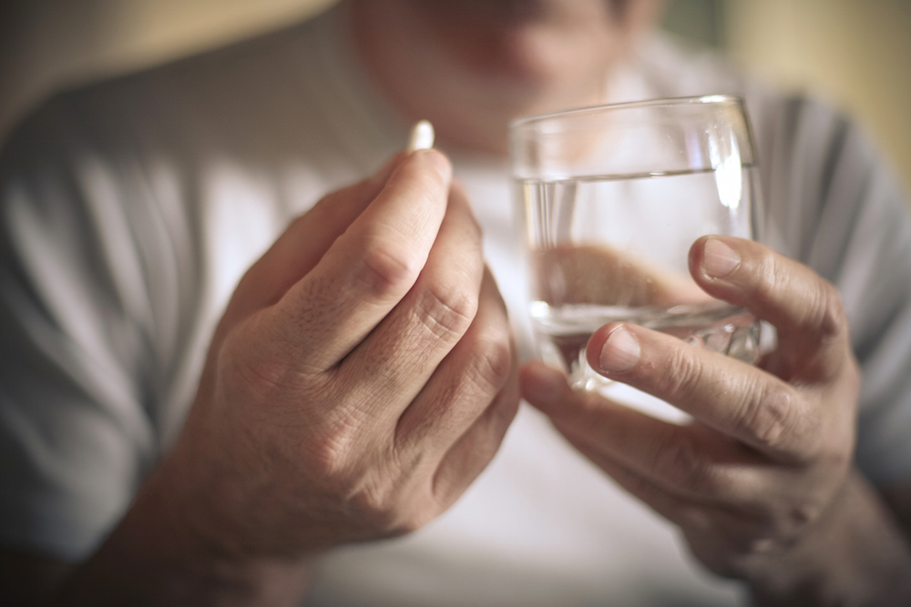 man holding a pill and a glass