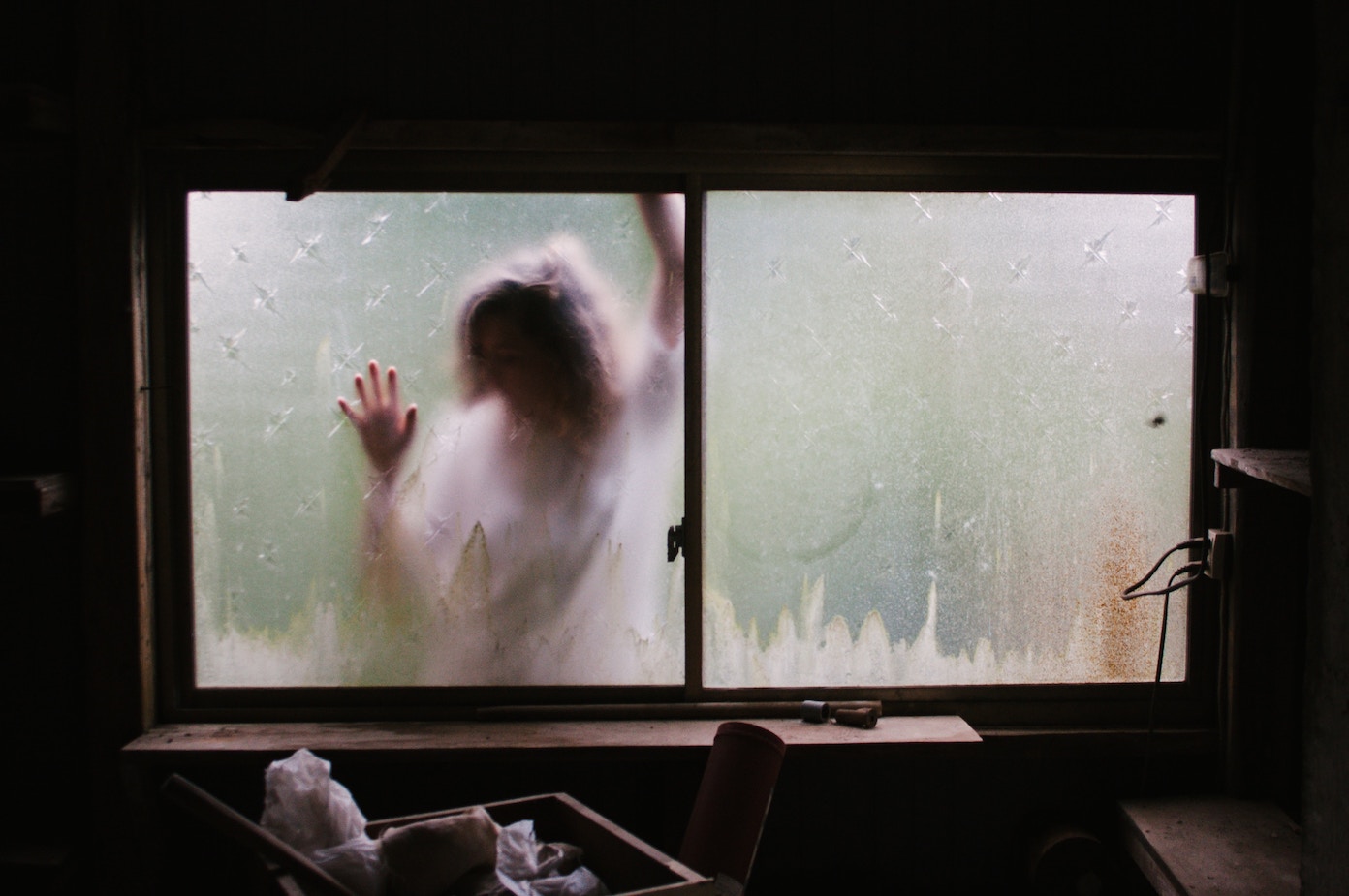 Blurry figure behind a window, pressing hands against the glass.