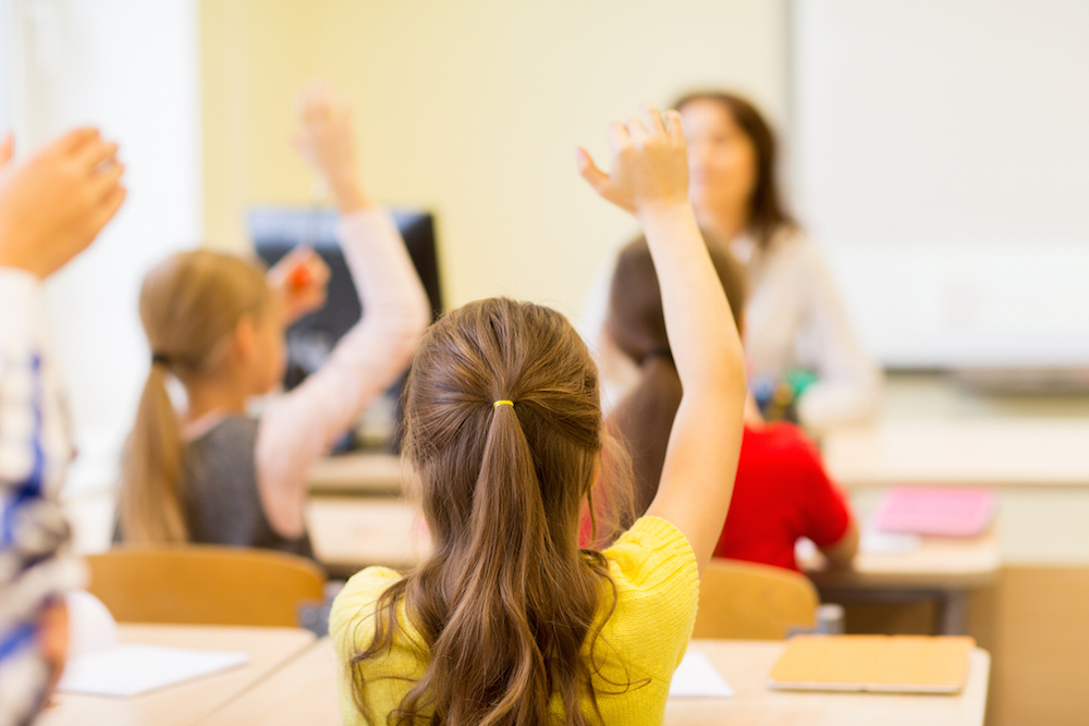kids raising their hands in a classroom