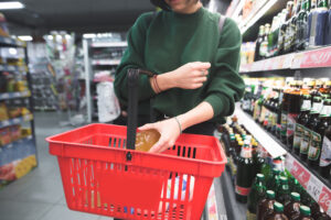 woman placing a bottle of alcohol in her shopping basket