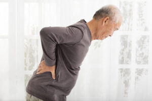 Older man bent over holding his back, chronic pain patients.