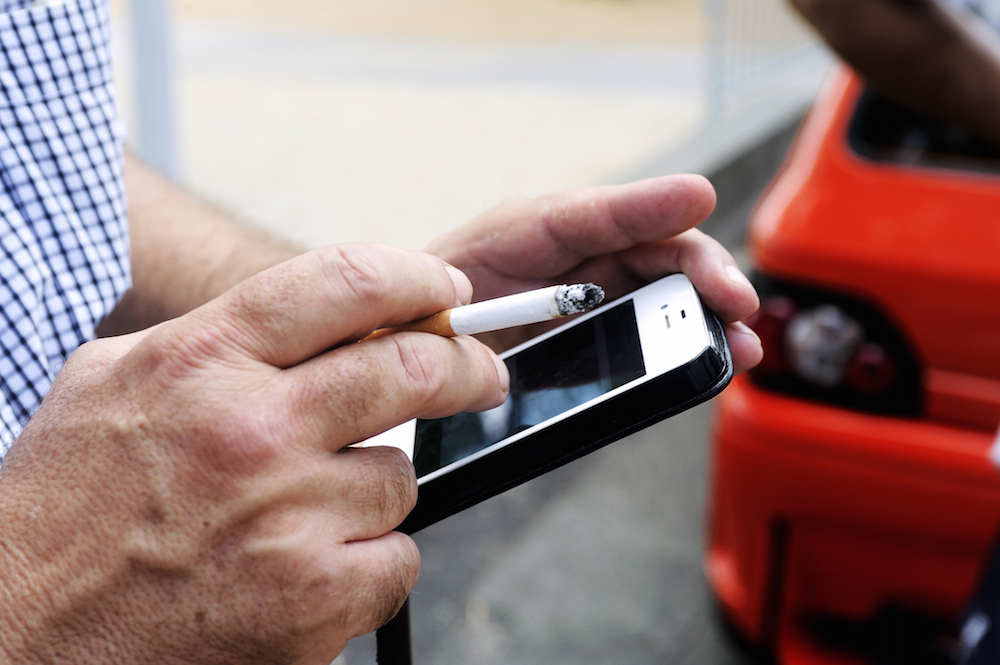 man smoking a cigarette while on his phone dealing with social media addiction