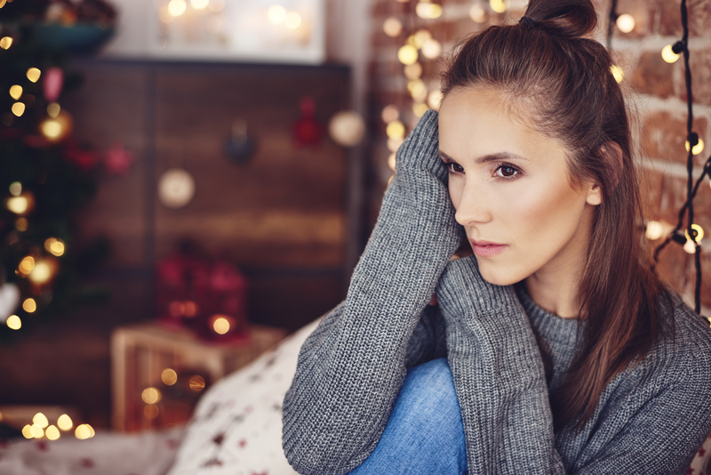 Woman with thoughtful expression, holiday lights behind her, sober holiday