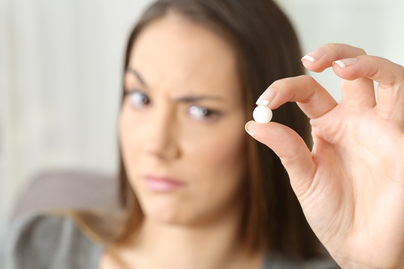 Woman holding pill in fingers, looking confused, thinking about opiate detox