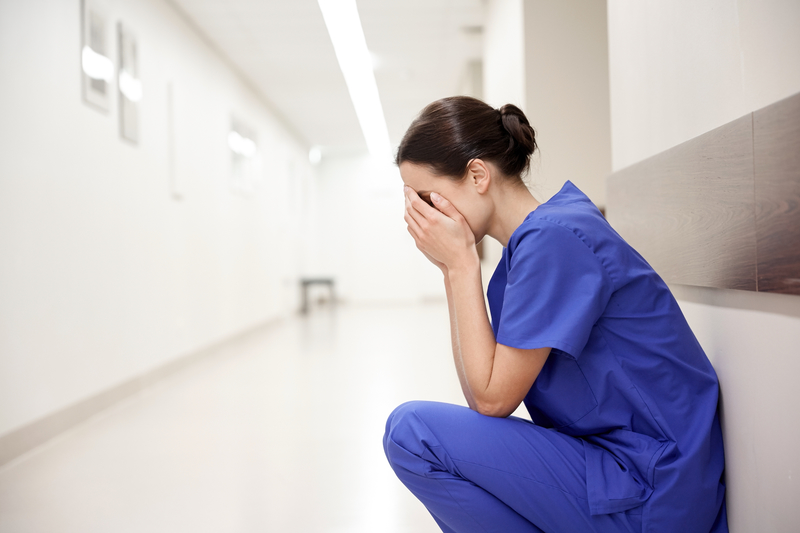 Woman in hospital scrubs sits on floor, head in hands, treatment professional relapse