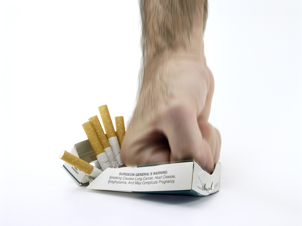 a hand crushing a pack of cigarettes that have a graphic image