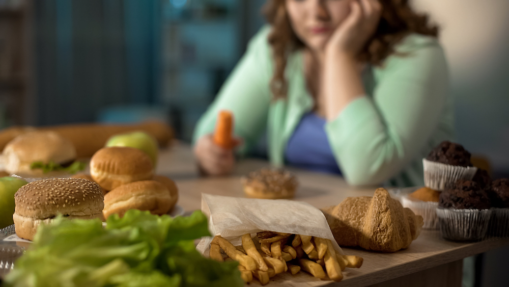 woman with binge eating disorder sitting in front of table full of food