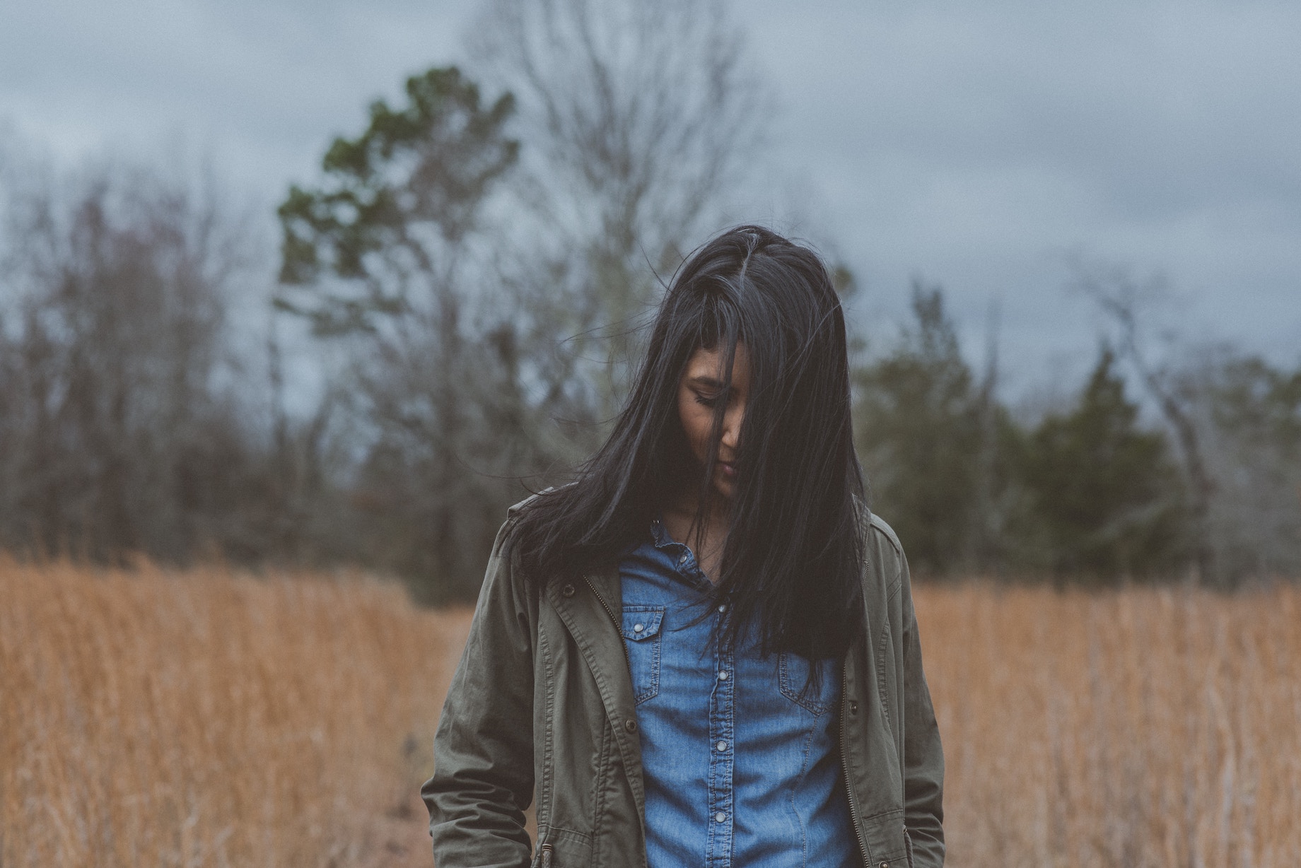 Woman in field with hair over face, looking down, contemplating psychiatric medication stigma