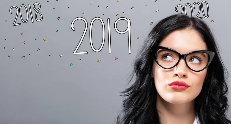 Woman wearing glasses looking up at the numbers 2019 in front of 2018 and 2020. Making New Year's resolutions