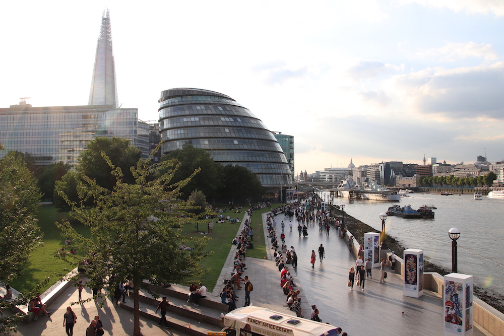 A landscape view of the River Thames with some of London`s modern architecture icons - London City Hall and The Shard, with people walking by the ricer