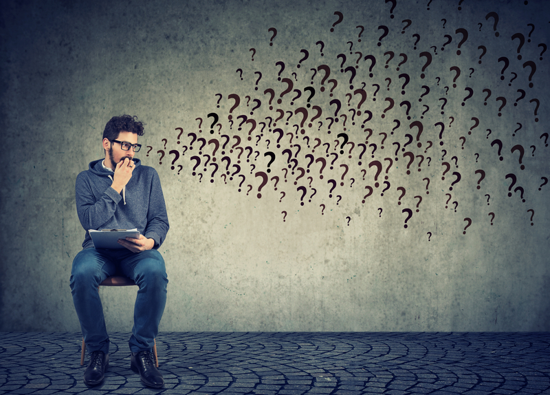 Man with felony drug charge sits on chair with question marks coming out of his head, concerned about how to get a job