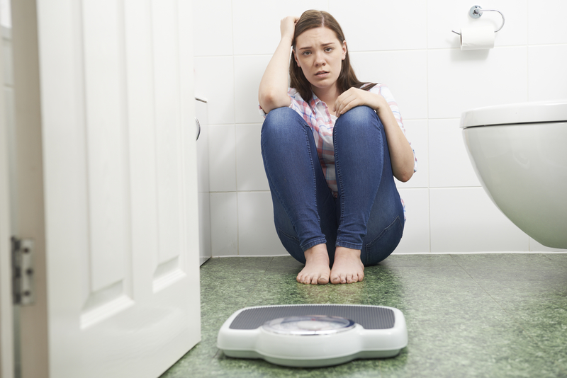 Woman on floor by toilet, with scale, upset and wanting eating disorder rehab