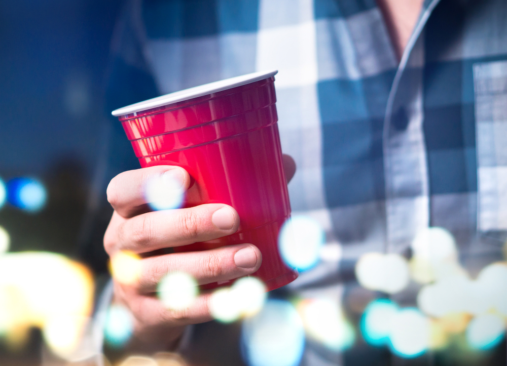 student with drunkorexia holding alcoholic beverage on college campus