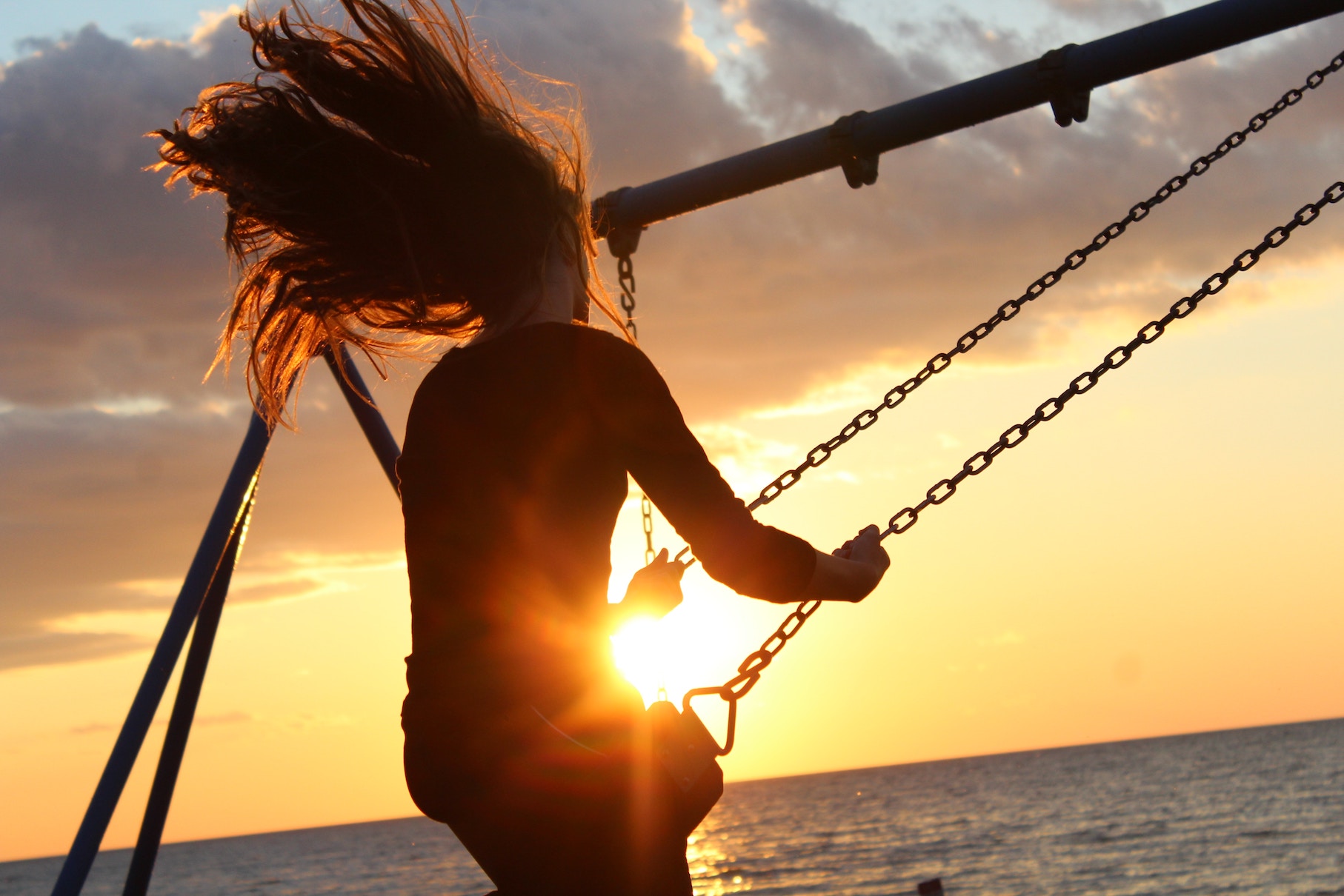 Woman on swing lit by sunset over ocean, mentally ill sister