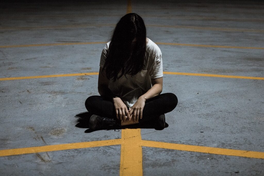 Are the 12 Steps Safe for Trauma Survivors? Woman sitting on ground in parking lot, trauma survivor