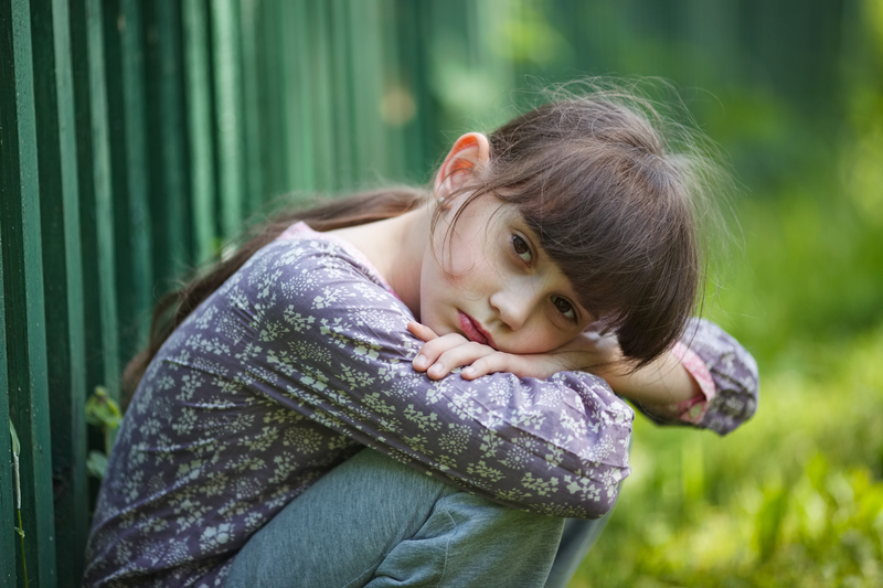 Little girl sitting with head resting on arms, sad about abusive mother and stepfather, wishing for her dad's protection