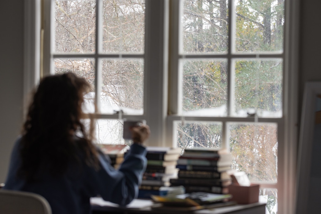Woman at desk looking out window, writer in recovery