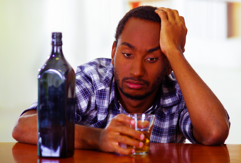 Miserable man sitting at bar with bottle and glass in front of him, alcohol relapse
