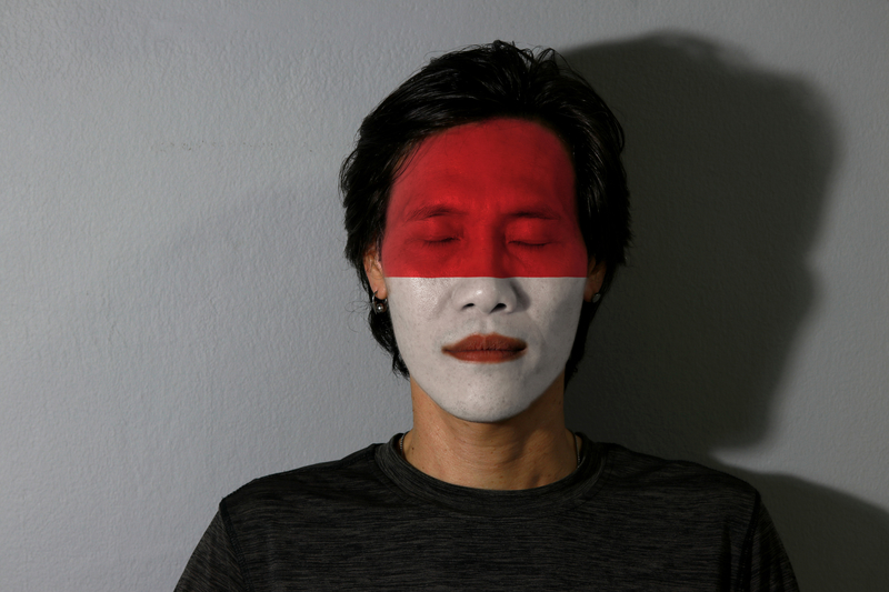 LGBTQ experience - young Indonesian man with eyes closed has Indonesian flag painted on his face