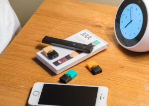Juul electronic cigarette sitting beside a phone and clock