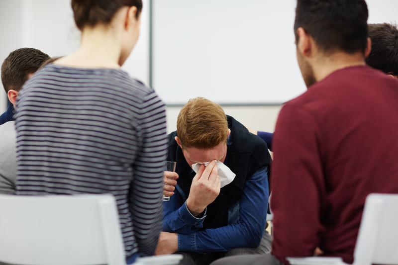 group sitting in a circle, one person grieving, head in hands.