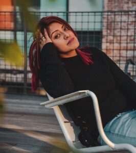 Woman sitting on white chair outside, relaxing, head on hand.