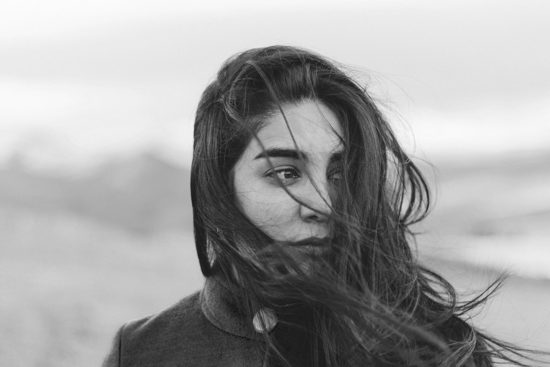 black and white image of woman, hair in wind across face, searching for something