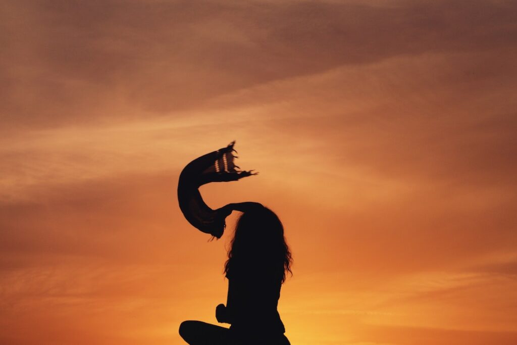 Person silhouetted against sunset, waving scarf in the air.
