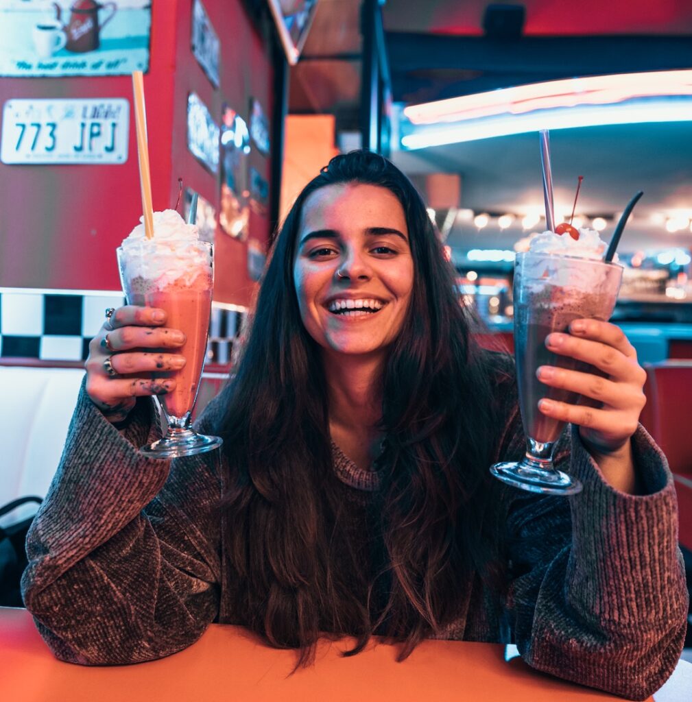 Woman holding two milkshakes in restaurant and smiling