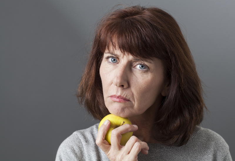Woman with chin on hand, holding apple.
